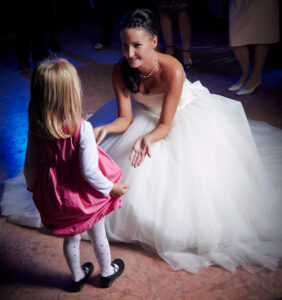 Menyasszony hófehér esküvői ruhában leguggol egy kislányhoz a táncparketten