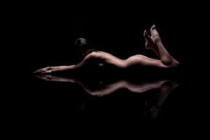 Aktmodell meztelenül hasal egy fekete tükröződő padlón